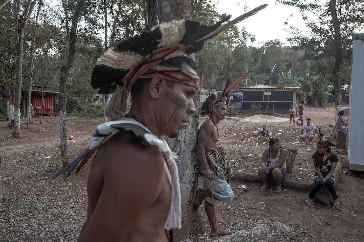 Um homem com cocar em pé na frente de um grupo de pessoas.