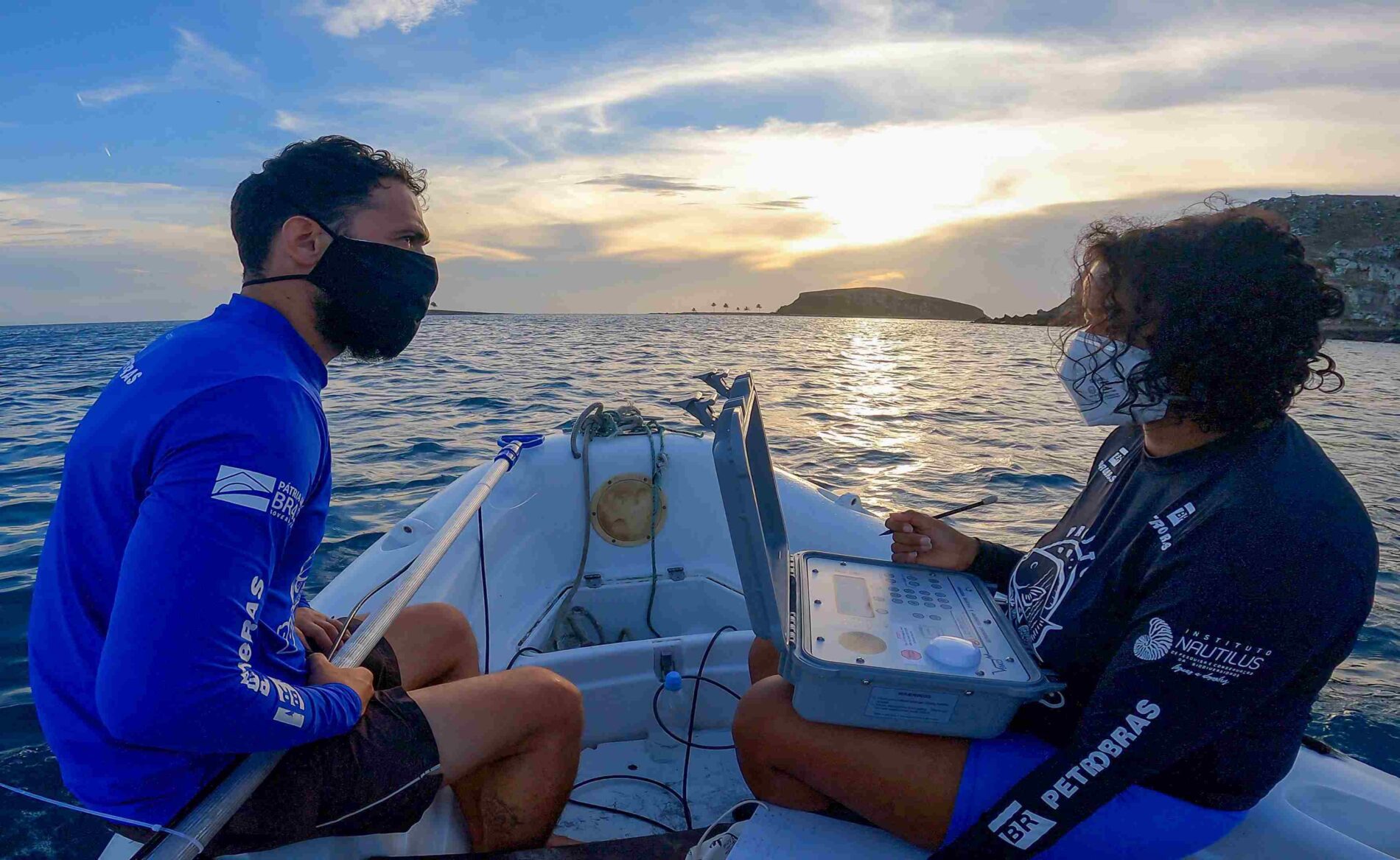 Duas pessoas de camisas azuis e máscaras sentadas em um barco.