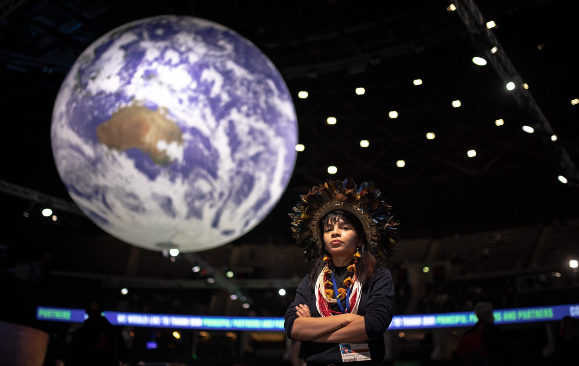 Uma mulher com um cocár na cabeça está em frente a um globo.