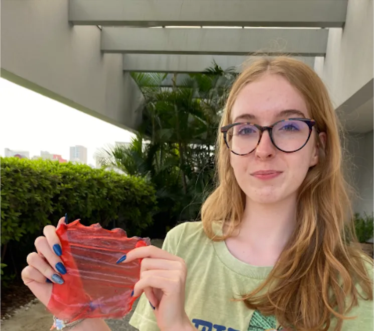 Uma garota com óculos segurando uma plástico biodegradável vermelho.