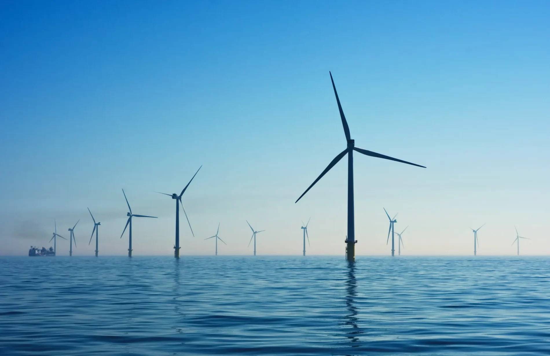 Imagem de turbinas eólicas no oceano com céu azul.