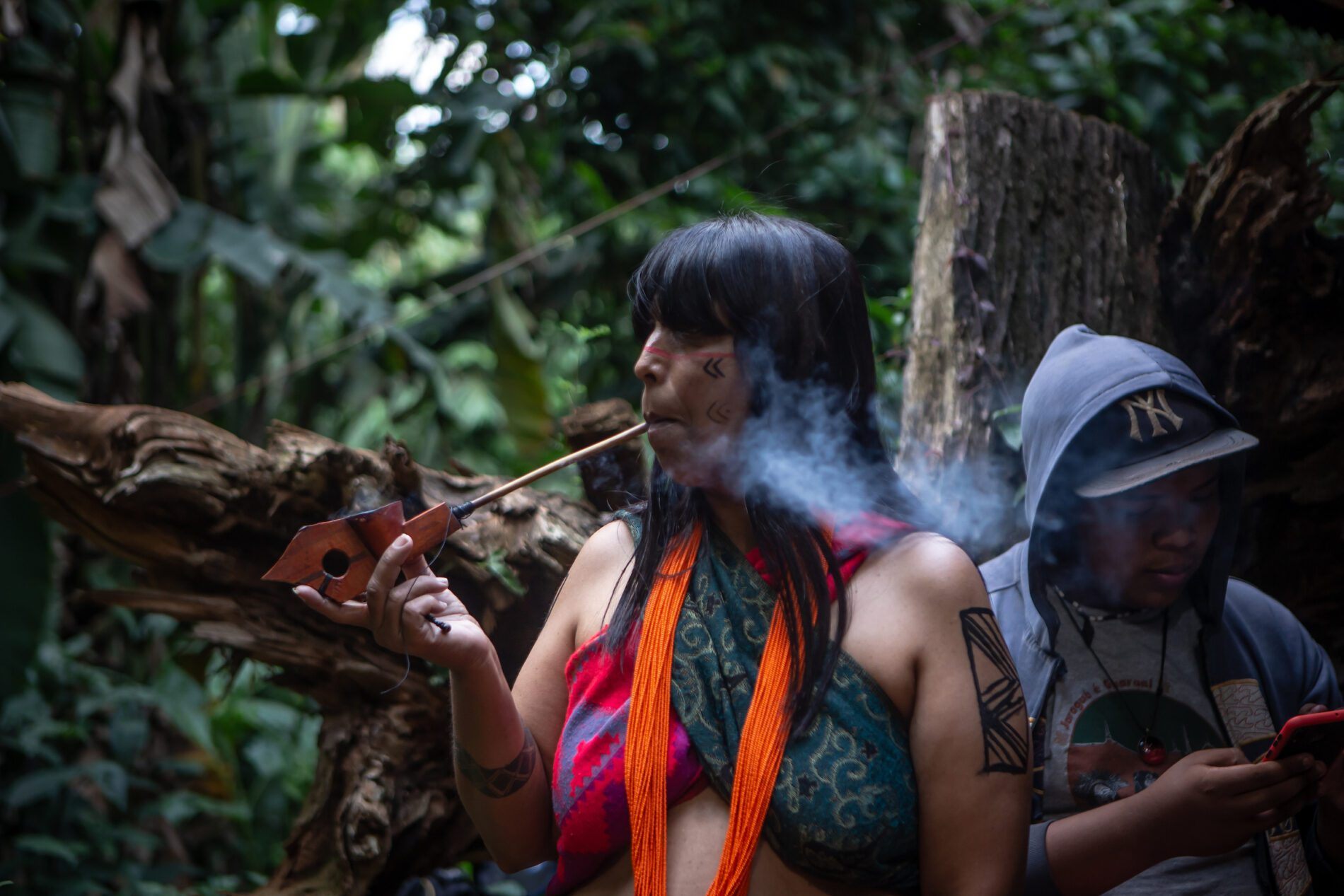 Uma mulher fumando cachimbo na floresta.