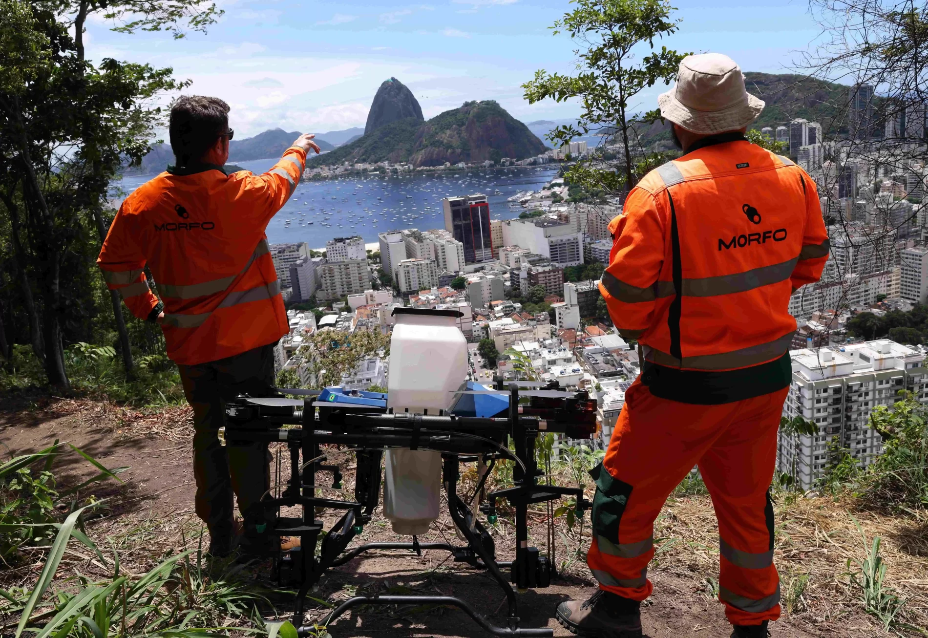 Dois homens preparam um drone semeador em uma área com vista para o Pão de Açúcar no Rio de Janeiro