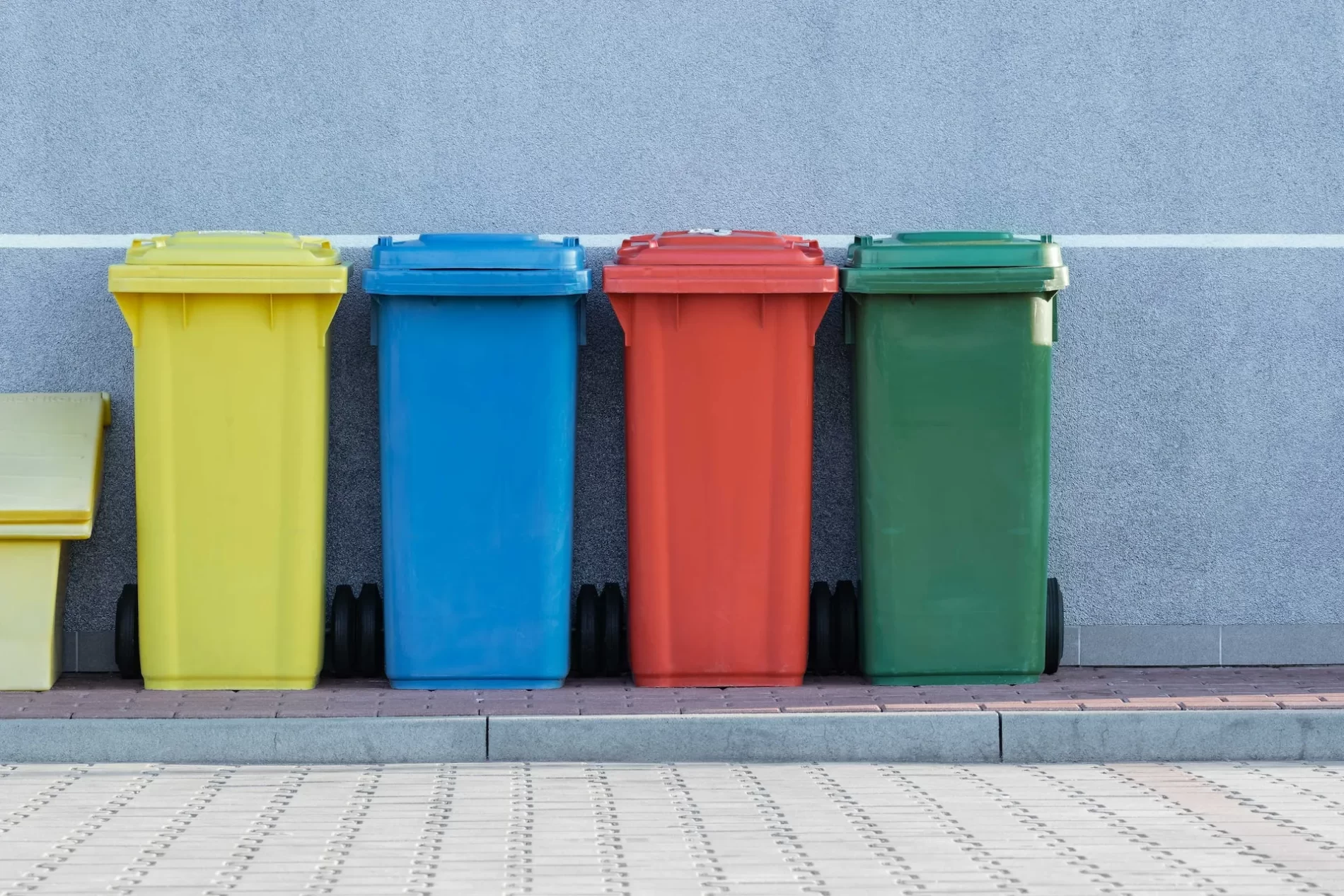 Imagem de uma fileira de latas de lixo coloridas alinhadas contra uma parede.